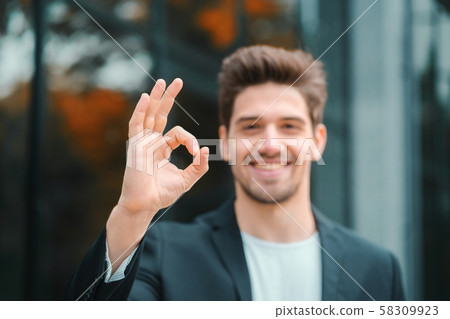 Successful man looking to camera and showing OK sign office building background 58309923