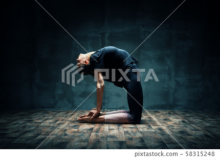 Young woman practicing yoga doing Camel pose in dark room 58315248