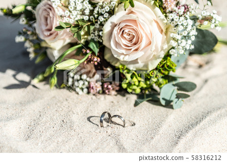Beautiful wedding rings lie in the sand surface at the beach against the background of a bride Beautiful wedding rings lie in the sand surface at the beach against the background of a bride 58316212