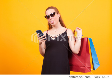 Cheerful young woman wearing sunglasses and holding colorful shopping bags 58316606