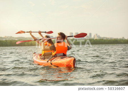 Happy couple kayaking on river with sunset on the background Happy couple kayaking on river with sunset on the background 58316607