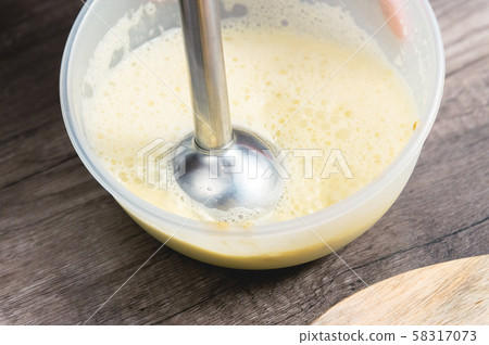 close-up whipping the mixture of homemade mayonnaise with a blender in a plastic bowl 58317073