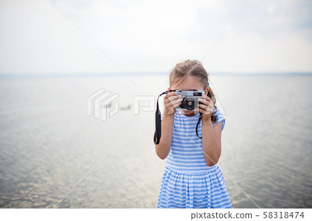 Front view of small girl with camera on a holiday by the lake, taking photos. Front view of small girl with camera on a holiday by the lake, taking photos. 58318474
