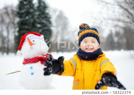 Little boy playing with funny snowman. Little boy playing with funny snowman. 58322374