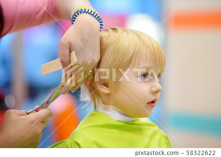 Preschooler boy getting haircut. Children hairdresser with professional tools - comb and scissors. 58322622