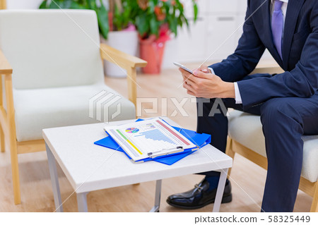 業務場景坐在辦公椅上同時操作智能手機的商人 業務場景坐在辦公椅上同時操作智能手機的商人 58325449