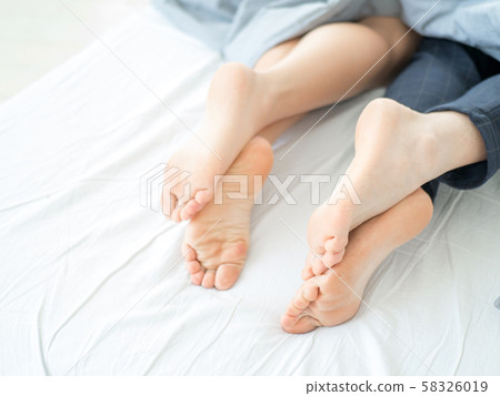 Couple lying in bed, sleeping under blanket, feet close up. 58326019