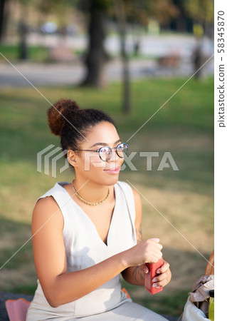 Woman wearing glasses sitting in park and opening healthy juice 58345870