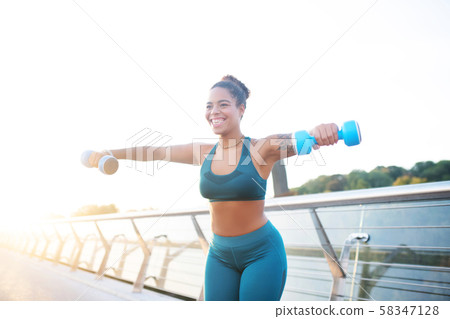Woman smiling while making exercises with barbells 58347128