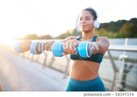 Woman holding blue barbells while building arm muscles 58347154