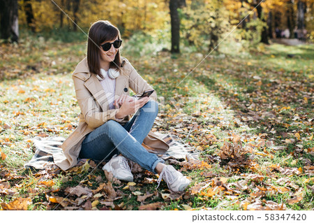 Young girl listening to music with headphones in the autumn forest Young girl listening to music with headphones in the autumn forest 58347420