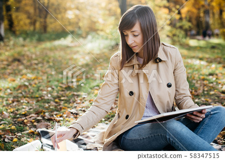 A young girl sketching near a lake in the autumn forest. Sketching A young girl sketching near a lake in the autumn forest. Sketching 58347515
