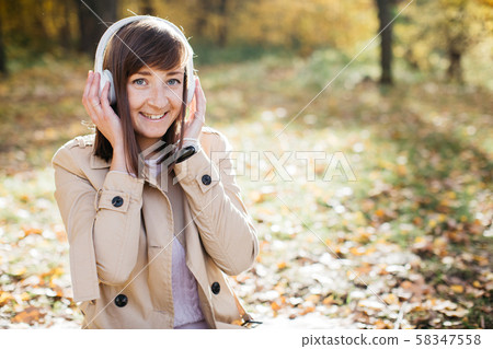 Young girl listening to music with headphones in the autumn forest Young girl listening to music with headphones in the autumn forest 58347558