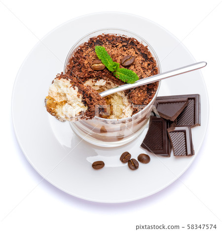 Classic tiramisu dessert in a glass cup on the plate and pieces of chocolate on white background Classic tiramisu dessert in a glass cup on the plate and pieces of chocolate on white background 58347574