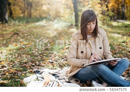 A young girl sketching near a lake in the autumn forest. Sketching 58347575