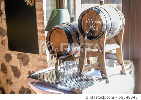 Old oak barrel with whiskey spirit small glases on a wooden table. in front of blurred background Old oak barrel with whiskey spirit small glases on a wooden table. in front of blurred background 58349345