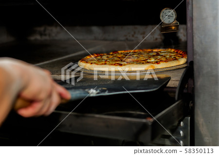 Chef taking pizza out of the oven with pizza shovel equipment. Chef taking pizza out of the oven with pizza shovel equipment. 58350113