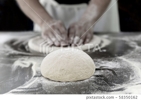 Ball of pizza dough on table with chef hands knead the dough in background. 58350162