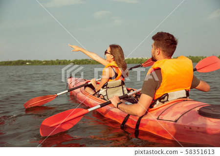 Happy couple kayaking on river with sunset on the background Happy couple kayaking on river with sunset on the background 58351613