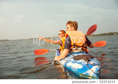 Happy couple kayaking on river with sunset on the background Happy couple kayaking on river with sunset on the background 58351614