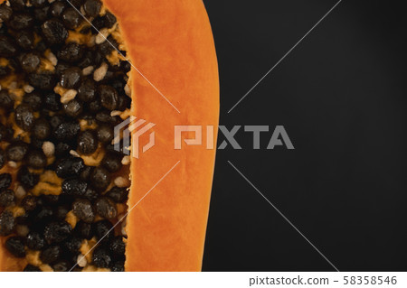 Half of ripe papaya with seed on a black plates and with a green plants on background. Slices of 58358546