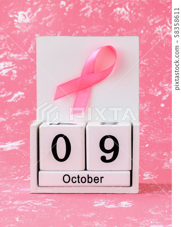 Pink ribbon of breast cancer awareness on a white wooden perpetual calendar with date 09 october.  58358611