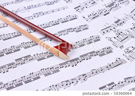 Brown violin bow on musical notes sheets. 58360064