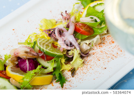 Tasty salad of boiled squids, lemon and lettuce leaves at plate 58364074