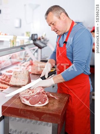 Smiling man seller cutting meat in shop 58366258