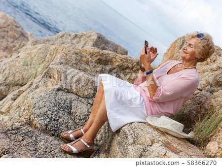 Elderly woman using phone at seaside Elderly woman using phone at seaside 58366270