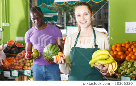 Smiling female seller is helping male client choose fresh fruits 58366320
