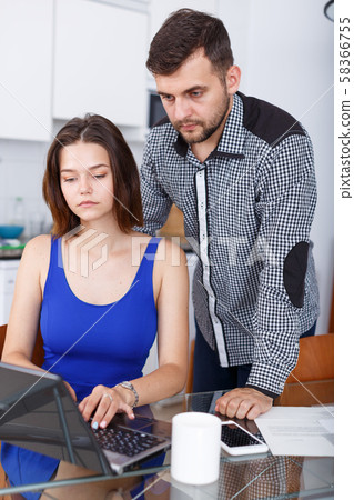 Woman looking at laptop with boyfriend at home interior Woman looking at laptop with boyfriend at home interior 58366755