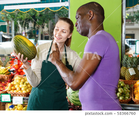 Smiling seller woman is helping man choose melone in the fruit market. 58366760