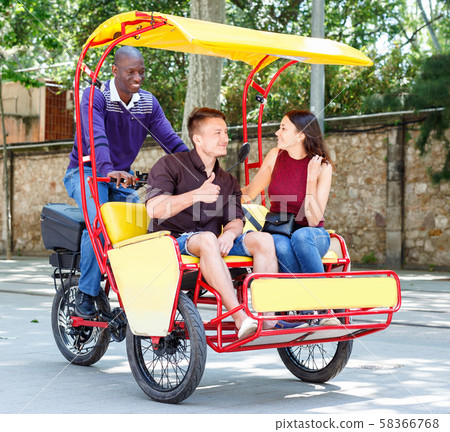 Young loving couple enjoying tour of city on trishaw with affable African American driver 58366768