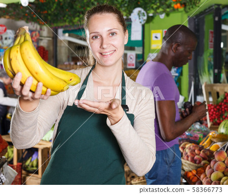 Portrait of seller woman who is standing with bananas on her workplace Portrait of seller woman who is standing with bananas on her workplace 58366773
