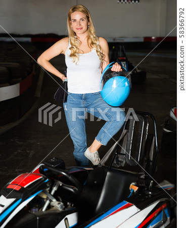 Smiling woman with helmet standing near cars for motor racing in sport club Smiling woman with helmet standing near cars for motor racing in sport club 58366792
