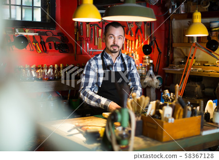 Hard-working man displaying his tools in leather workshop 58367128