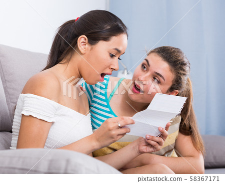 Teenagers girls reading letter on couch Teenagers girls reading letter on couch 58367171