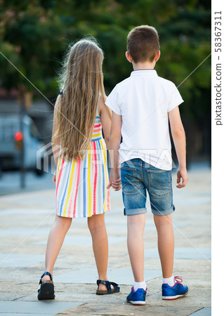 Two kids walking together in town, view from back Two kids walking together in town, view from back 58367311