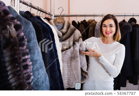 Woman choosing short coffee-colored fur jacket in women’s cloths store Woman choosing short coffee-colored fur jacket in women’s cloths store 58367787