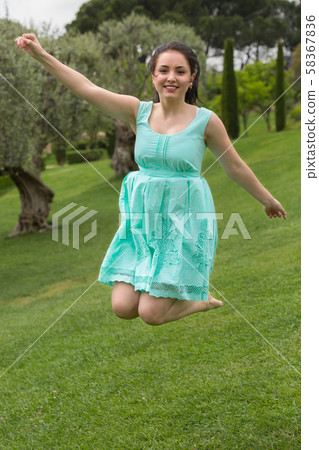 positive young brunette girl in dress jumping at the garden positive young brunette girl in dress jumping at the garden 58367836