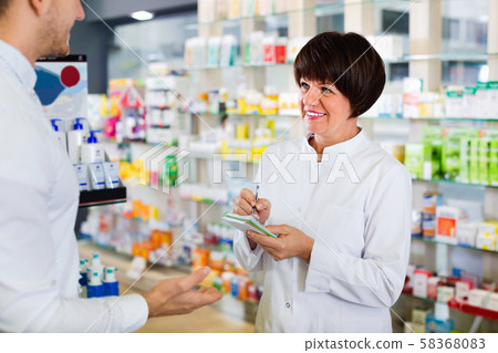 Woman pharmacist helping customers in drug store Woman pharmacist helping customers in drug store 58368083