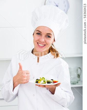 portrait of young coosie woman showing salad at kitchen 58368413