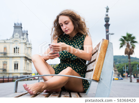 Sexy woman tourist in dress sitting at wooden bench in historical center Sexy woman tourist in dress sitting at wooden bench in historical center 58368420