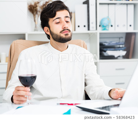 Man holding glass of red wine and working Man holding glass of red wine and working 58368423