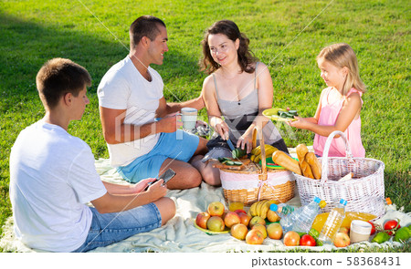 Parents with two teenagers enjoying delicious meal on the picnic Parents with two teenagers enjoying delicious meal on the picnic 58368431