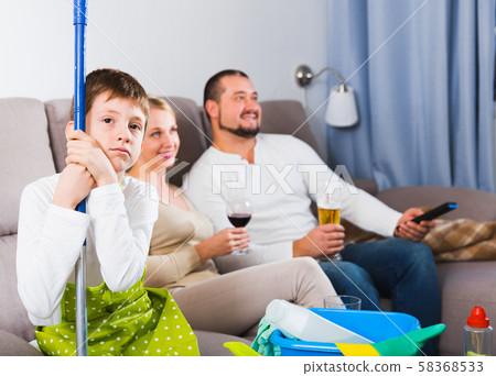 Sad boy tired after cleaning with carefree parents Sad boy tired after cleaning with carefree parents 58368533