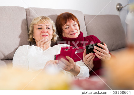 Two senior women with phones on sofa Two senior women with phones on sofa 58368604