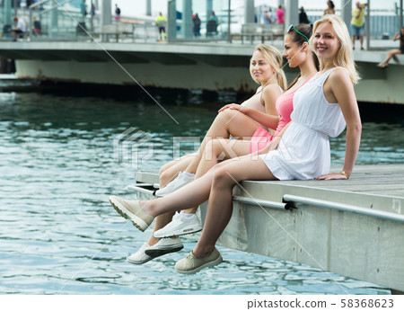 Girls sitting on harbour sidewalk 58368623