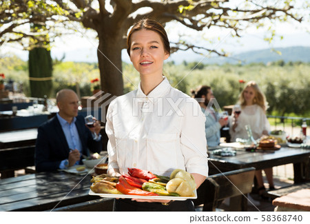 Positive woman waiter demonstrating open-air restaurant to visitors Positive woman waiter demonstrating open-air restaurant to visitors 58368740